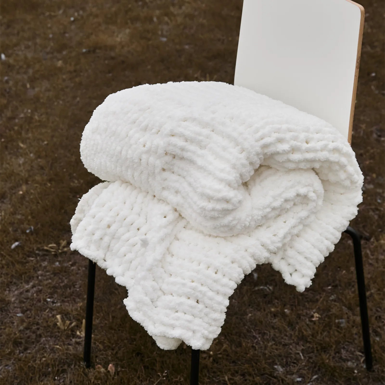 A neatly folded white chunky knit blanket resting on a chair outdoors, showing its plush, durable texture.