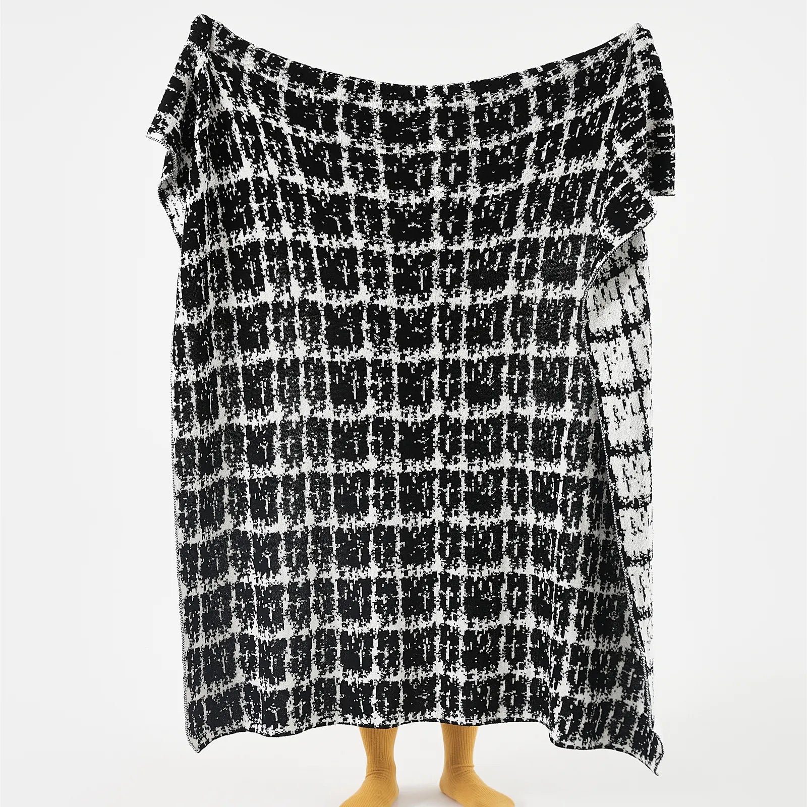 A person holding up the full-sized artistic black and white wool blanket to display the complete, abstract grid pattern.