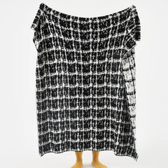 A person holding up the full-sized artistic black and white wool blanket to display the complete, abstract grid pattern.