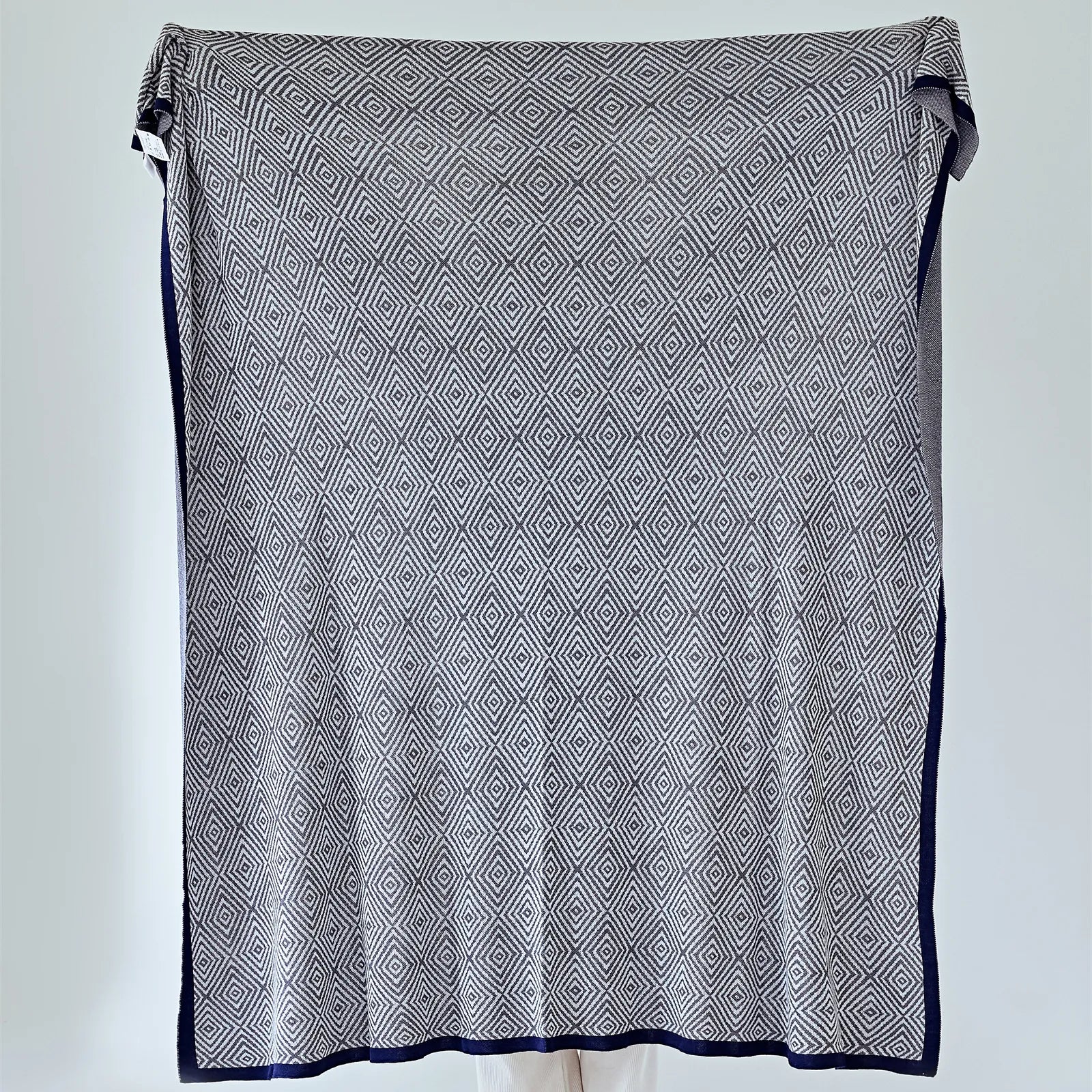 Full view of the large charcoal-grey diamond pattern throw with a navy-blue border, held up for display.