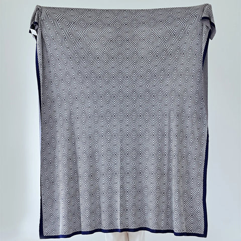 Full view of the large charcoal-grey diamond pattern throw with a navy-blue border, held up for display.