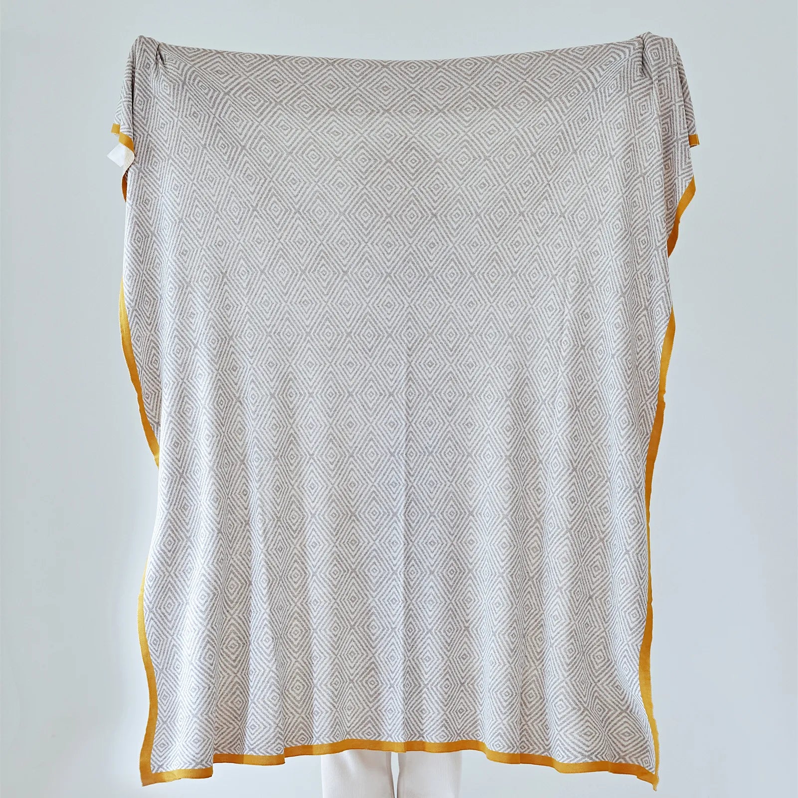 Full view of the large light-grey diamond pattern throw with a striking mustard-yellow border, held up for display.