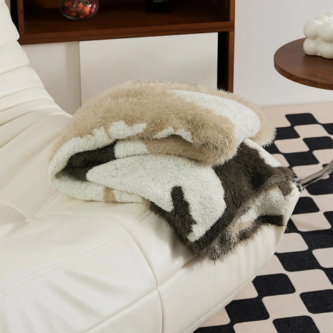 Close up detail shot of fluffy abstract knit throw blanket in taupe resting on white sofa armrest
