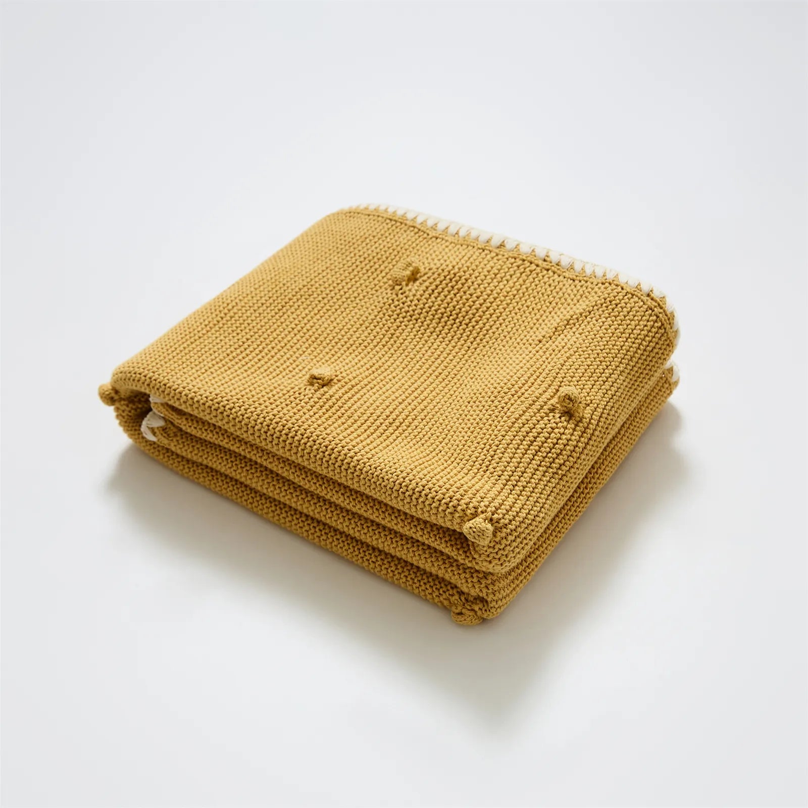 Neatly folded ginger yellow cotton knit throw with cream fringe trim and bobble texture