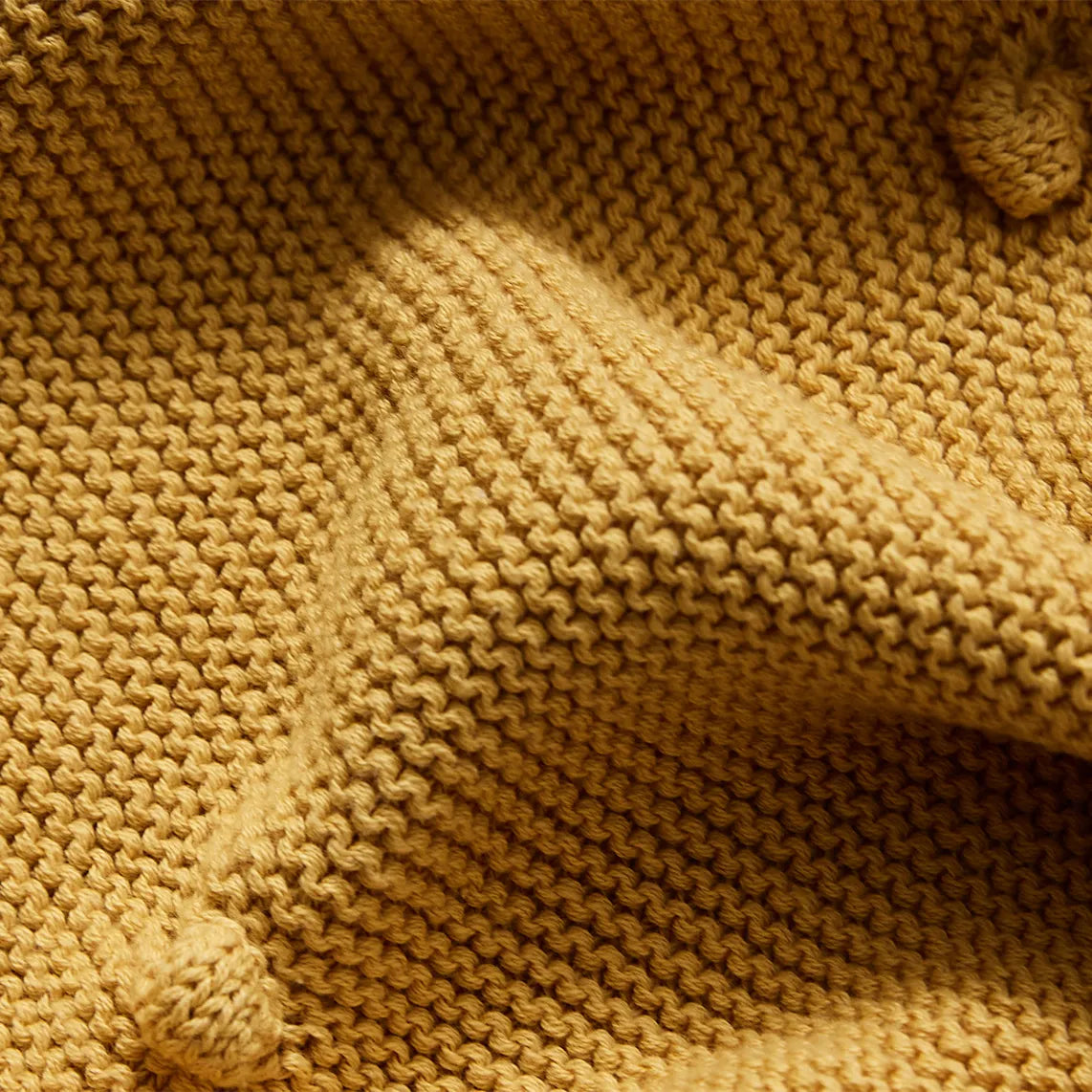 Close up detail of the textured ginger yellow cotton knit fabric showing the bobble pattern
