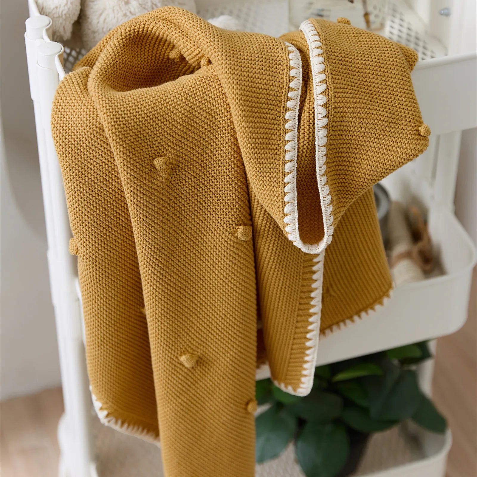 Ginger yellow cotton knit throw draped over white rolling cart with green houseplant