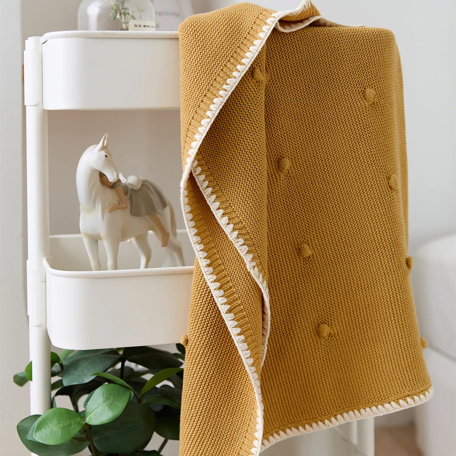 Ginger yellow cotton bobble throw hanging on white storage cart with unicorn figurine