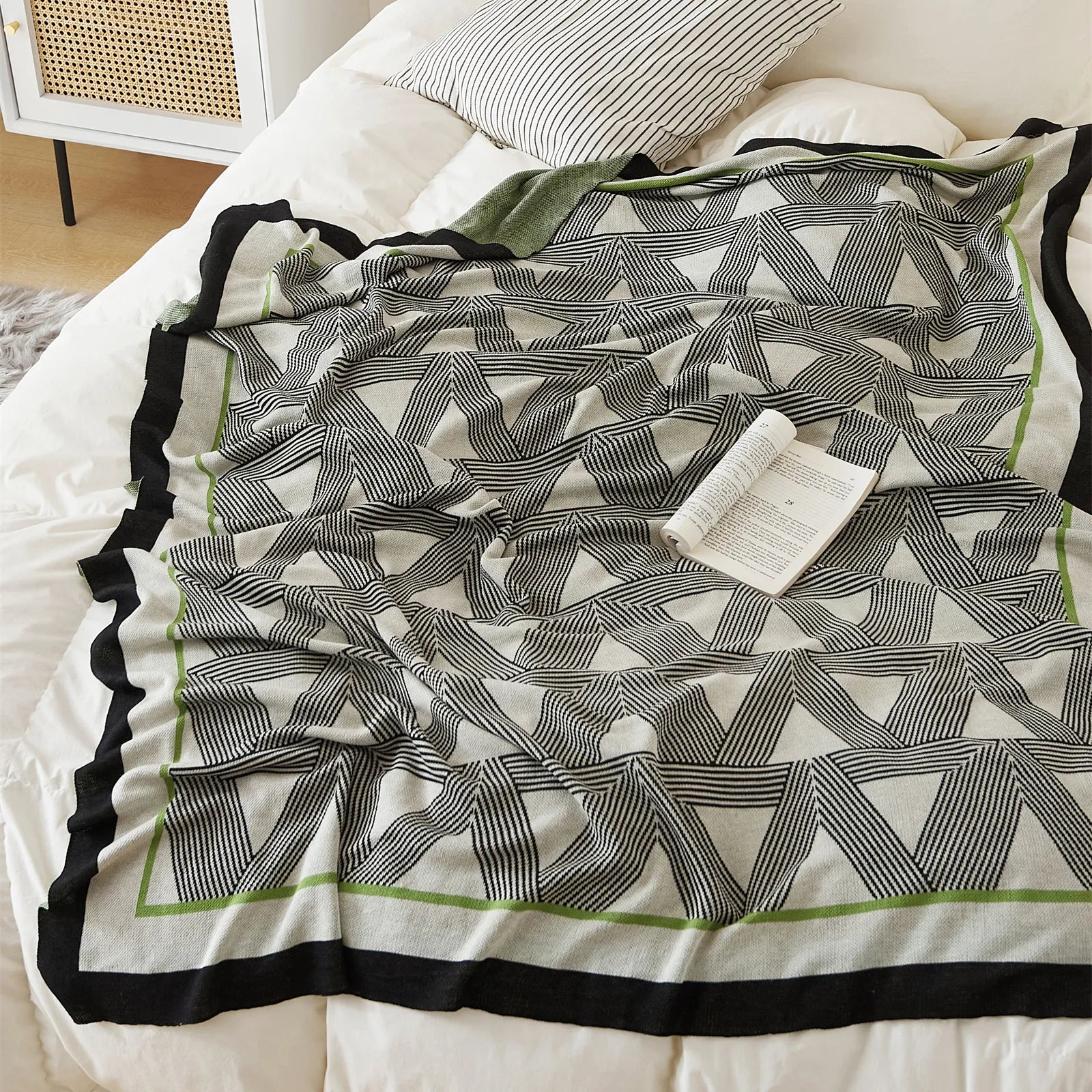 A close-up view of the geometric throw blanket on a white bed, showing its striking pattern and elegant border.