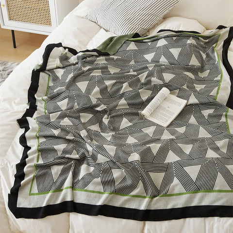 A close-up view of the geometric throw blanket on a white bed, showing its striking pattern and elegant border.