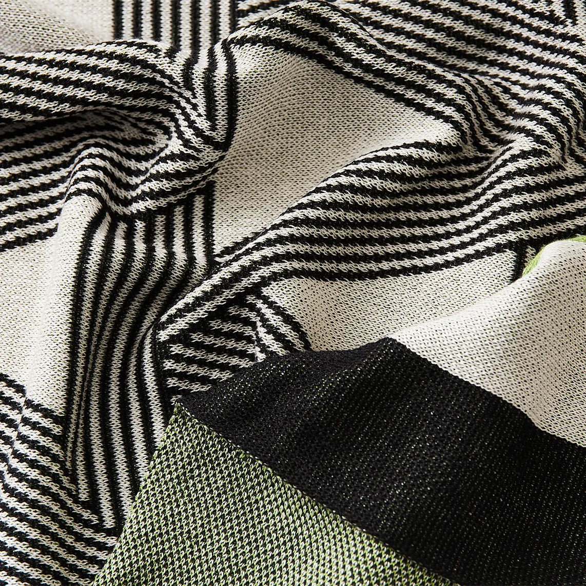 close-up view of the geometric throw blanket on a white bed, showing its striking pattern and elegant border