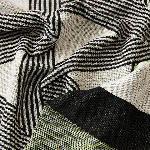 close-up view of the geometric throw blanket on a white bed, showing its striking pattern and elegant border
