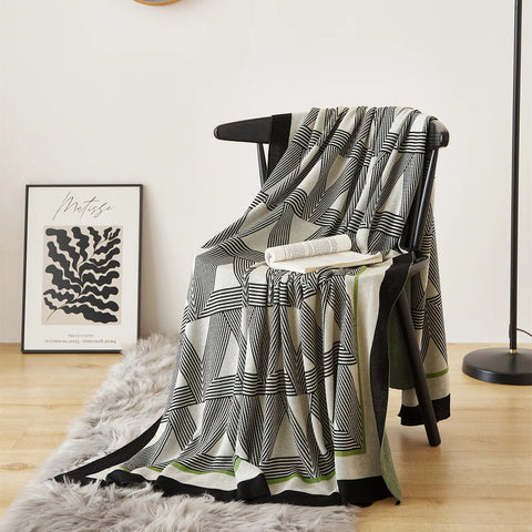 A black and white geometric blanket with a green border draped over a black chair in a modern room.