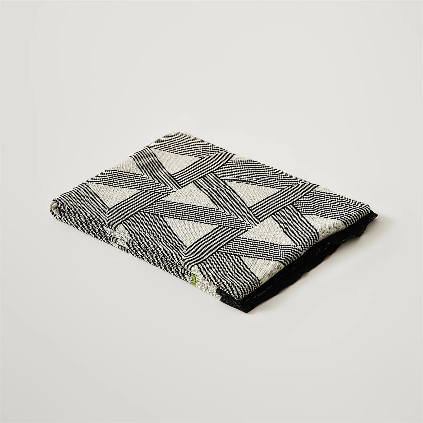 A studio shot of a perfectly folded geometric blanket, showcasing its clean design and green accents.