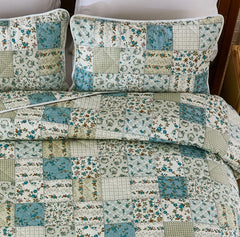 Overhead close-up of the patchwork quilt showing blue and green floral and checkered patterns.
