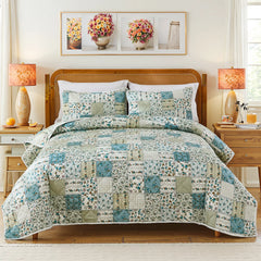 A complete bedroom scene featuring a bed with a green and blue patchwork quilt set, two lamps, and wall art.
