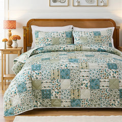 Full view of a bed with a green and blue patchwork quilt set, wood headboard, and matching lamps.