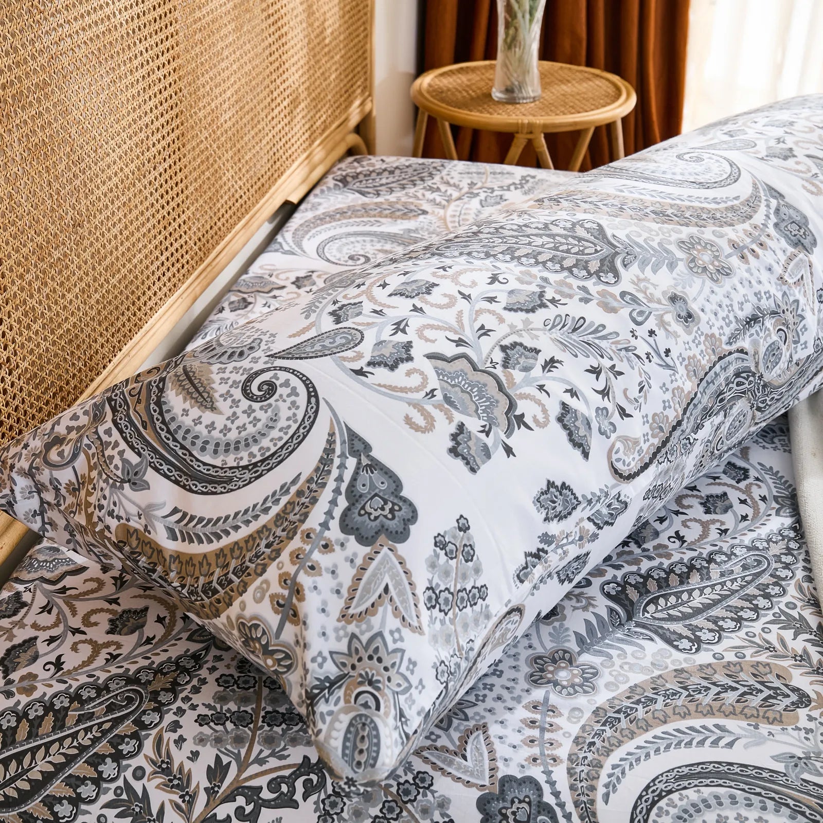A side-angled view of a long grey paisley cotton pillowcase on a bed, showing its full length and how it complements the bedding.