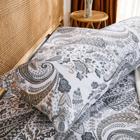 A side-angled view of a long grey paisley cotton pillowcase on a bed, showing its full length and how it complements the bedding.