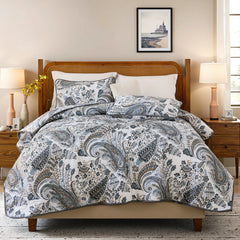 Full view of the grey paisley quilt set styled on a bed in a bright bedroom