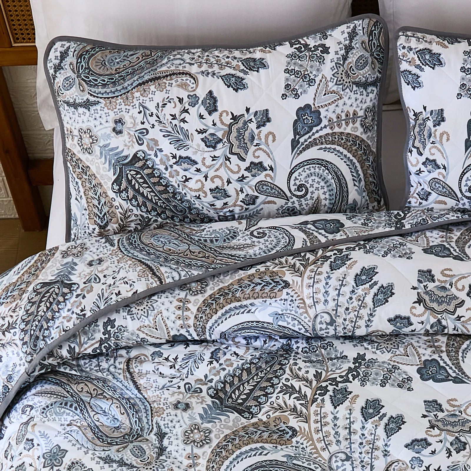 The grey paisley quilt set on a bed with decorative pillows and shams.