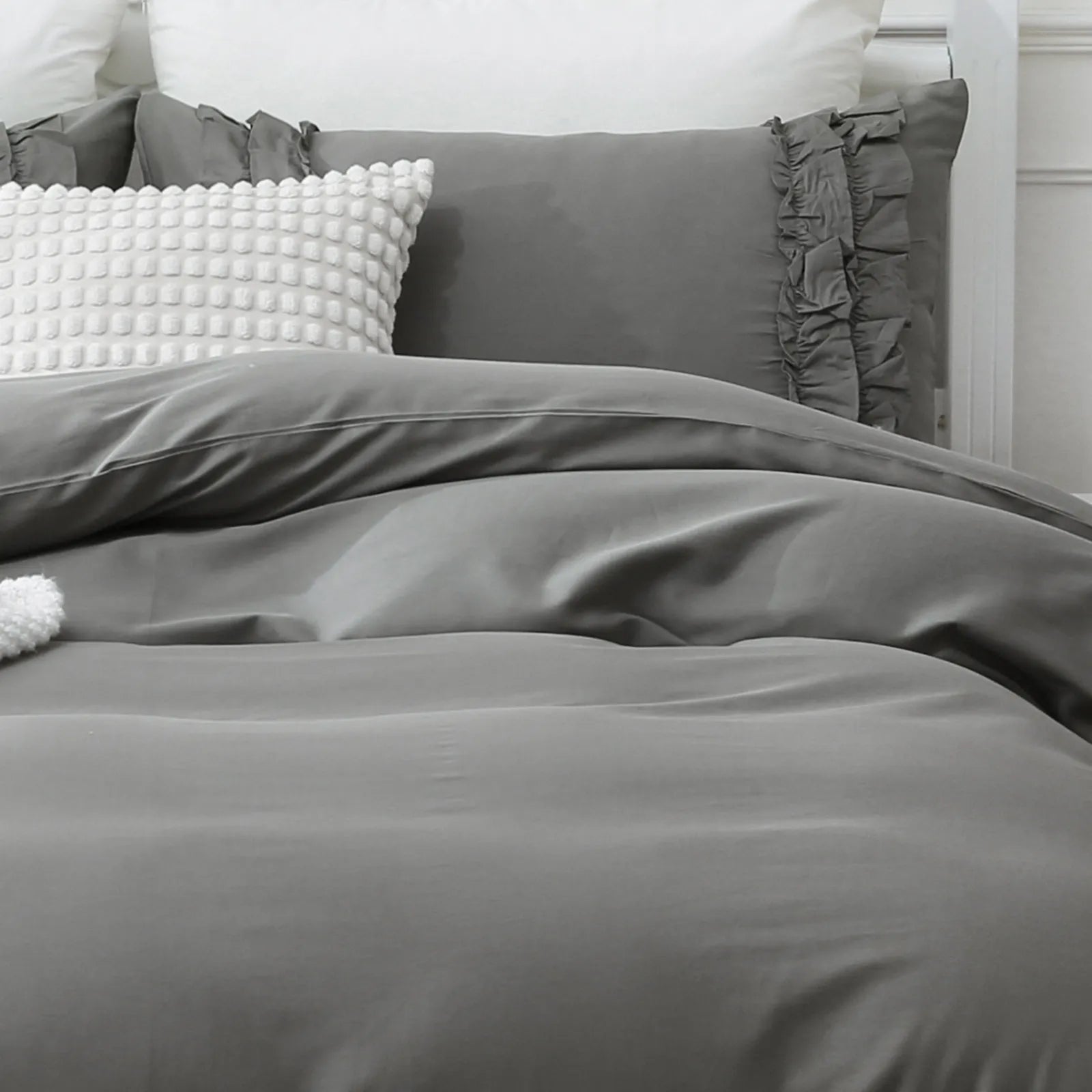 the  grey ruffled comforter set styled on a bed in a bright bedroom.