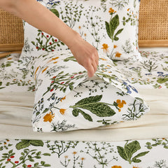 A hand gently pulls open the end of a white cotton botanical print pillowcase, revealing the inner details and quality.