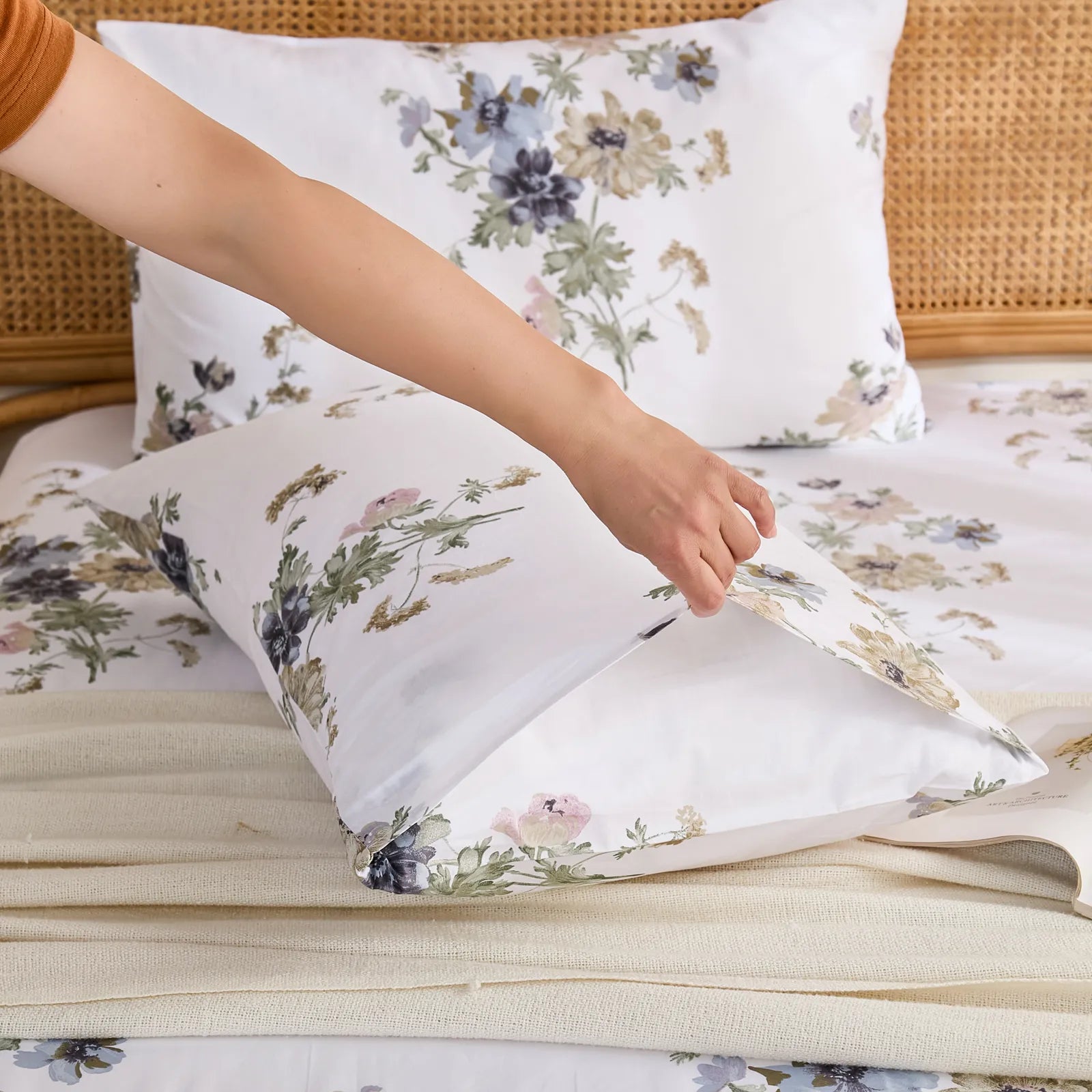 Hand Placing Cotton Floral Pillowcase onto Bed with Wicker Headboard