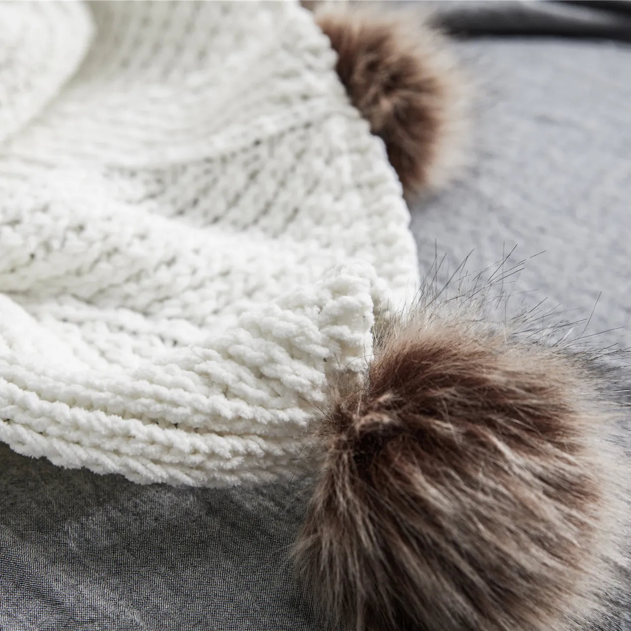 Detail of soft ivory knit fabric with large brown faux fur pom-pom corner