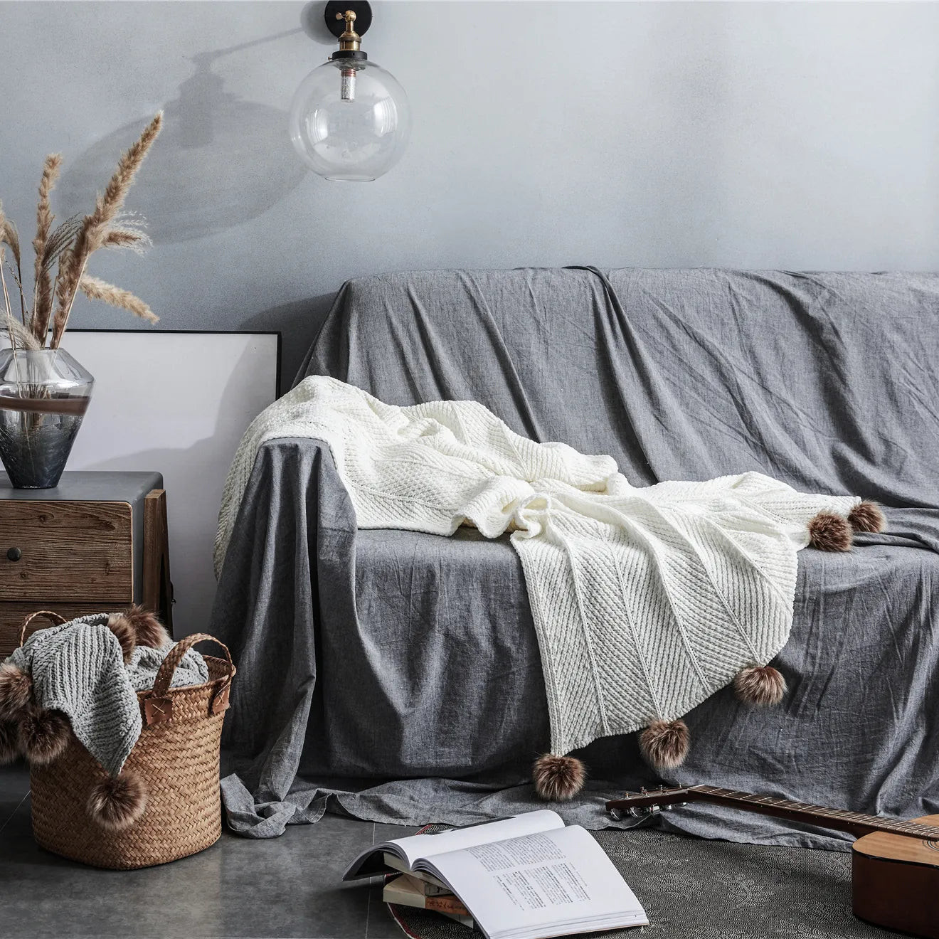 Ivory pom-pom throw draped on grey sofa in cozy living room setting