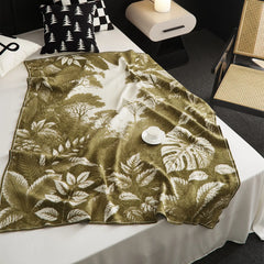 The green Forest-Inspired landscape blanket draped over a bed, with a stack of books for a calm and cozy reading nook.
