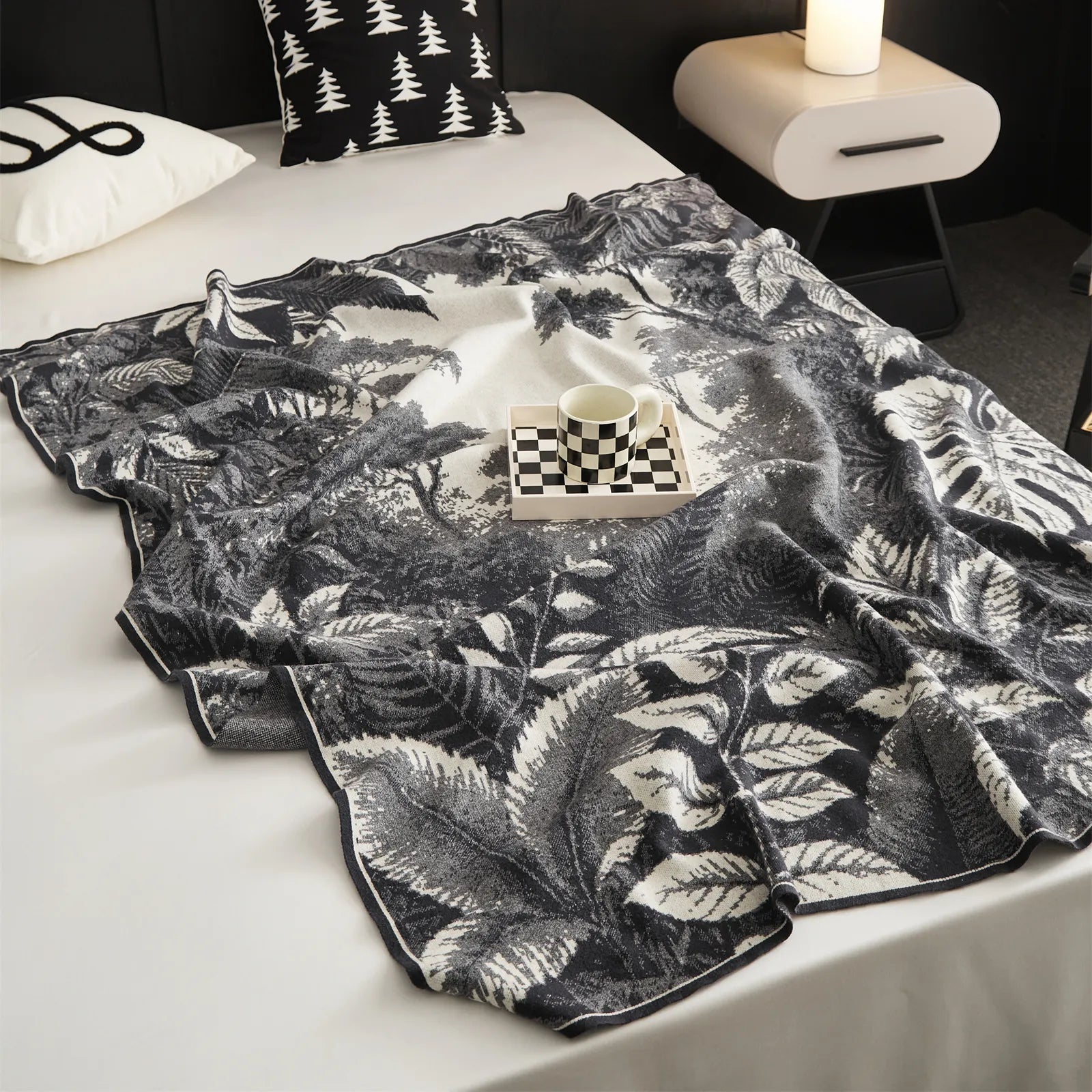 The grey Forest-Inspired landscape blanket draped over a bed, with a stack of books for a calm and cozy reading nook.