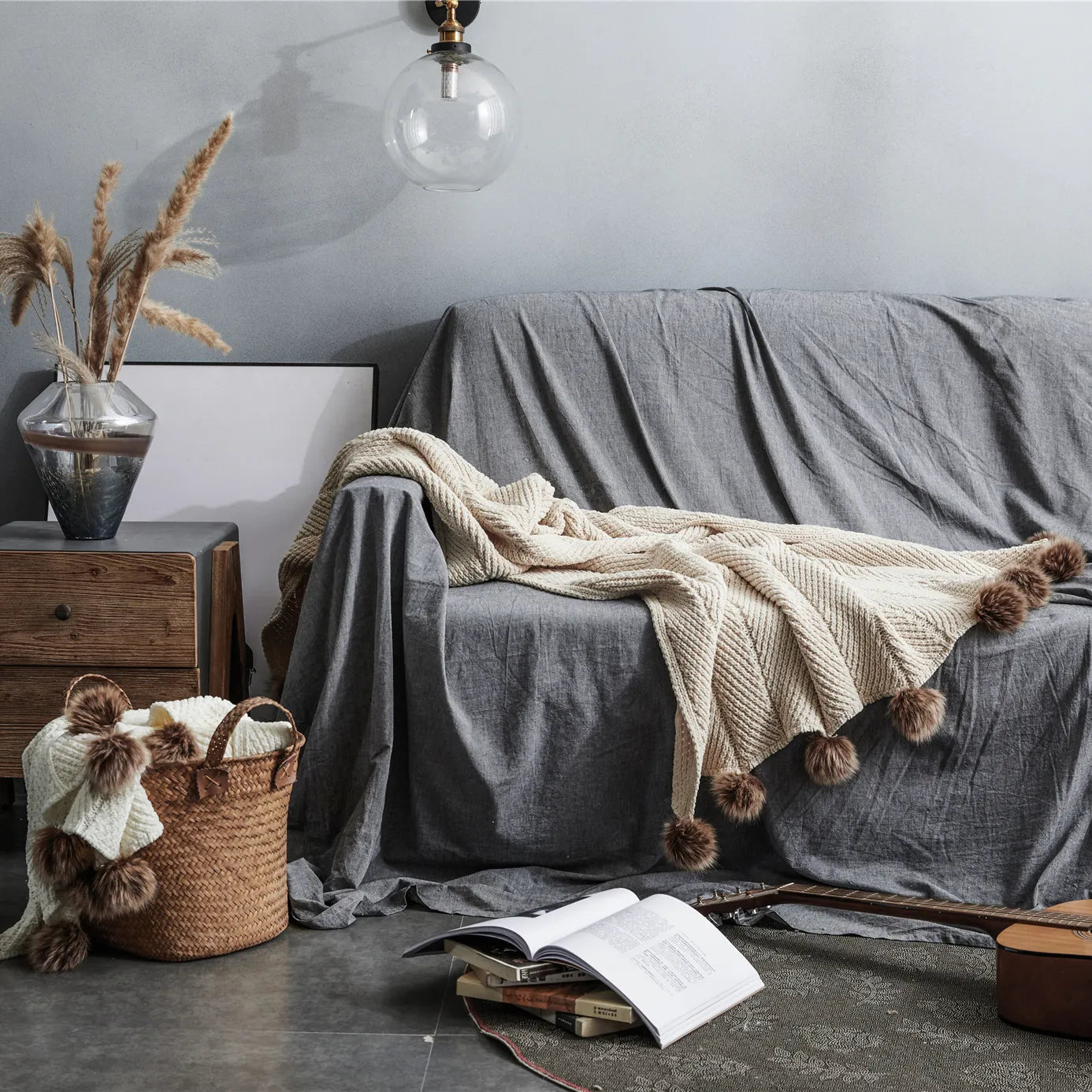 Light beige pom-pom throw draped on grey sofa in bohemian home decor setting