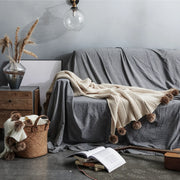 Light beige pom-pom throw draped on grey sofa in bohemian home decor setting