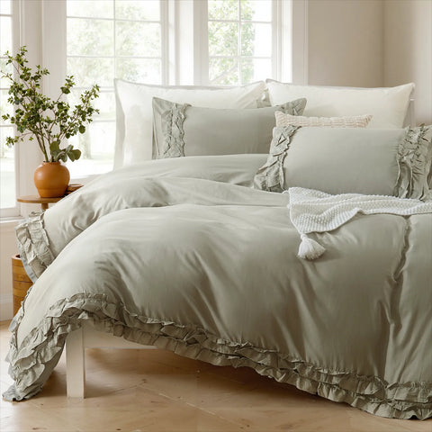Light gray cotton double ruffle duvet cover set with a tassel pillow, beside a brown vase and a window with tree views.