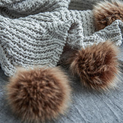 Detail of soft light heather grey knit fabric with two large brown faux fur pom-poms