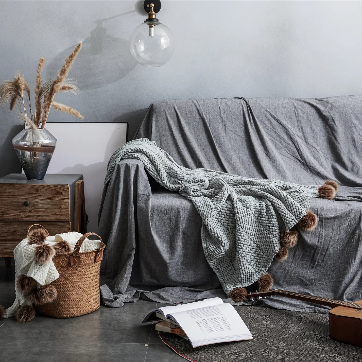 Light heather grey pom-pom throw draped on dark grey sofa in stylish living room