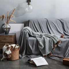 Light heather grey pom-pom throw draped on dark grey sofa in stylish living room