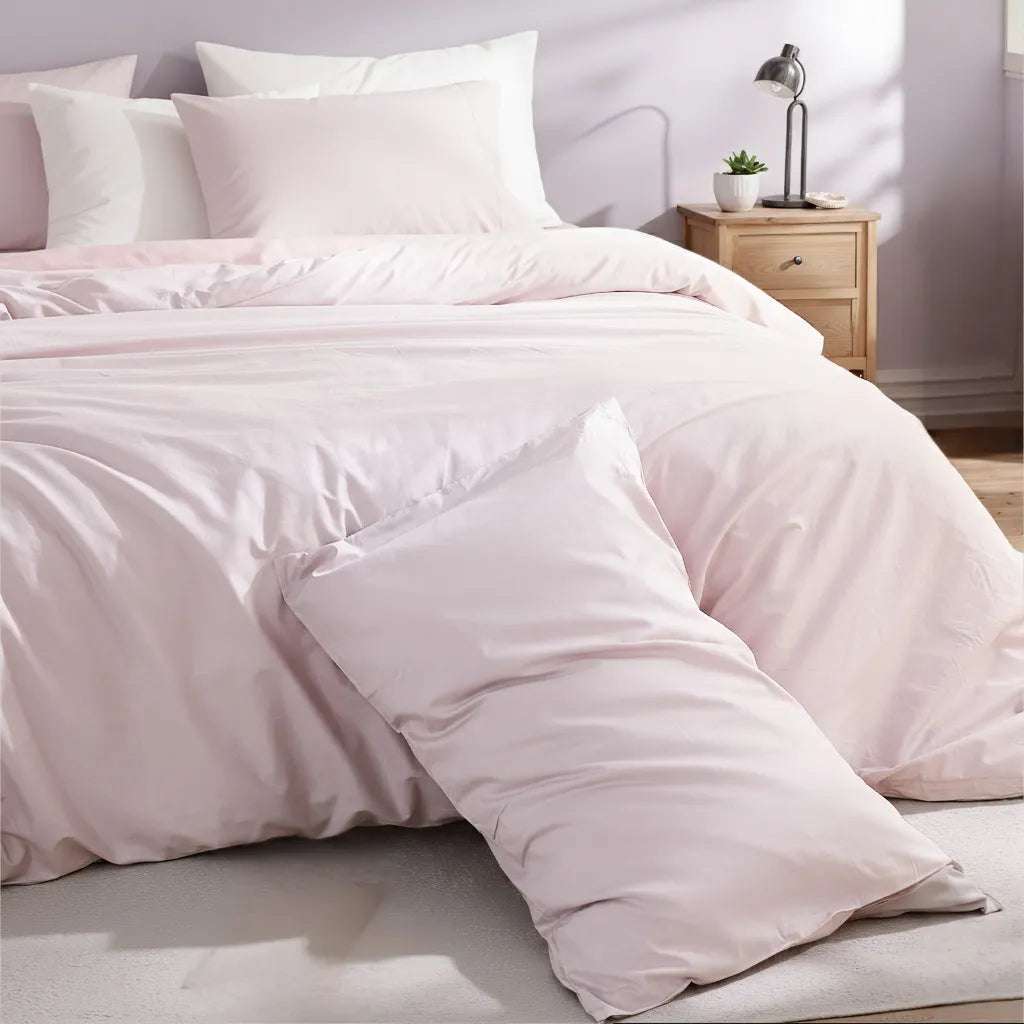 Angled view of light purple duvet with casually leaning pillow, metal lamp and small potted plant on nightstand.