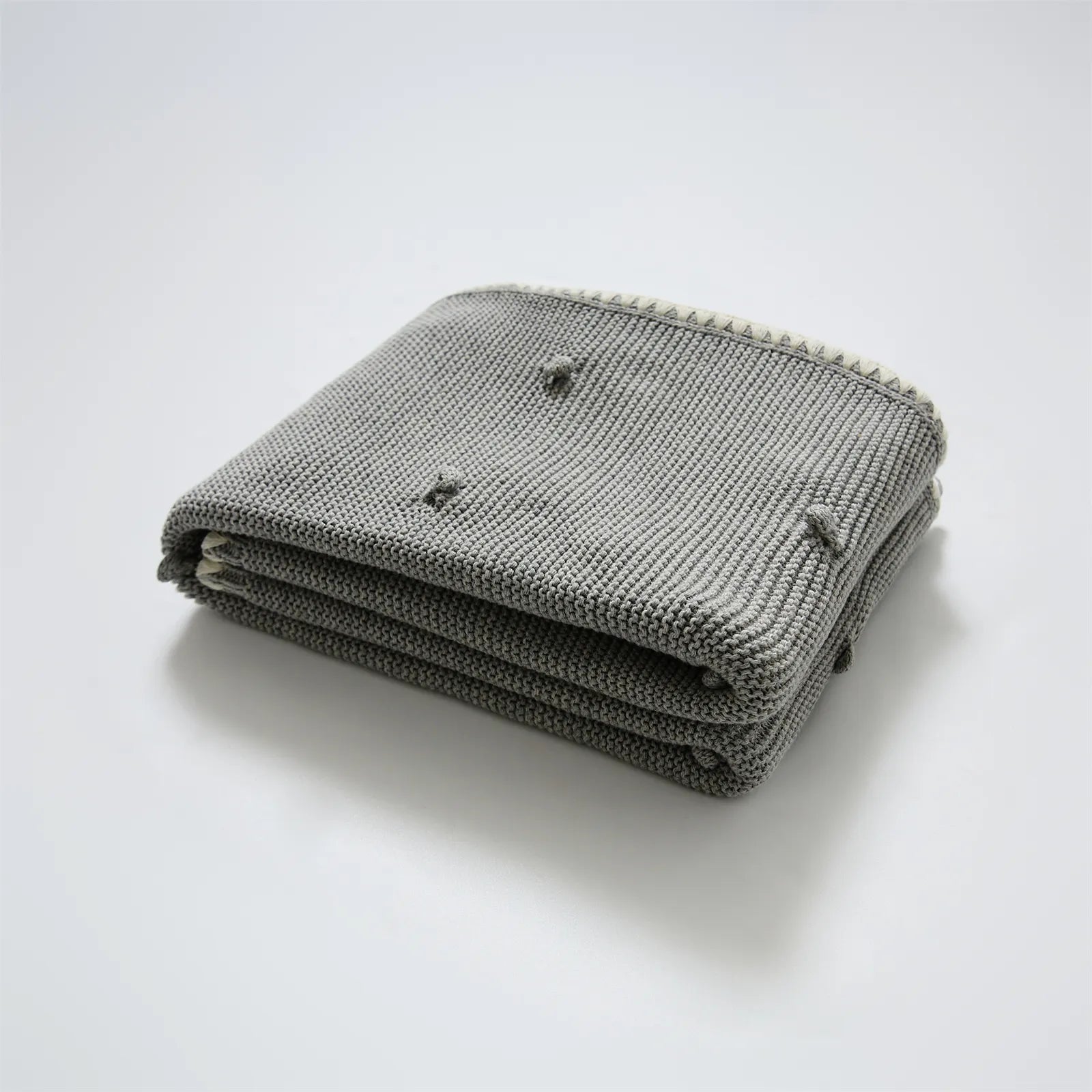 Neatly folded medium grey cotton knit throw with cream fringe trim and bobble texture