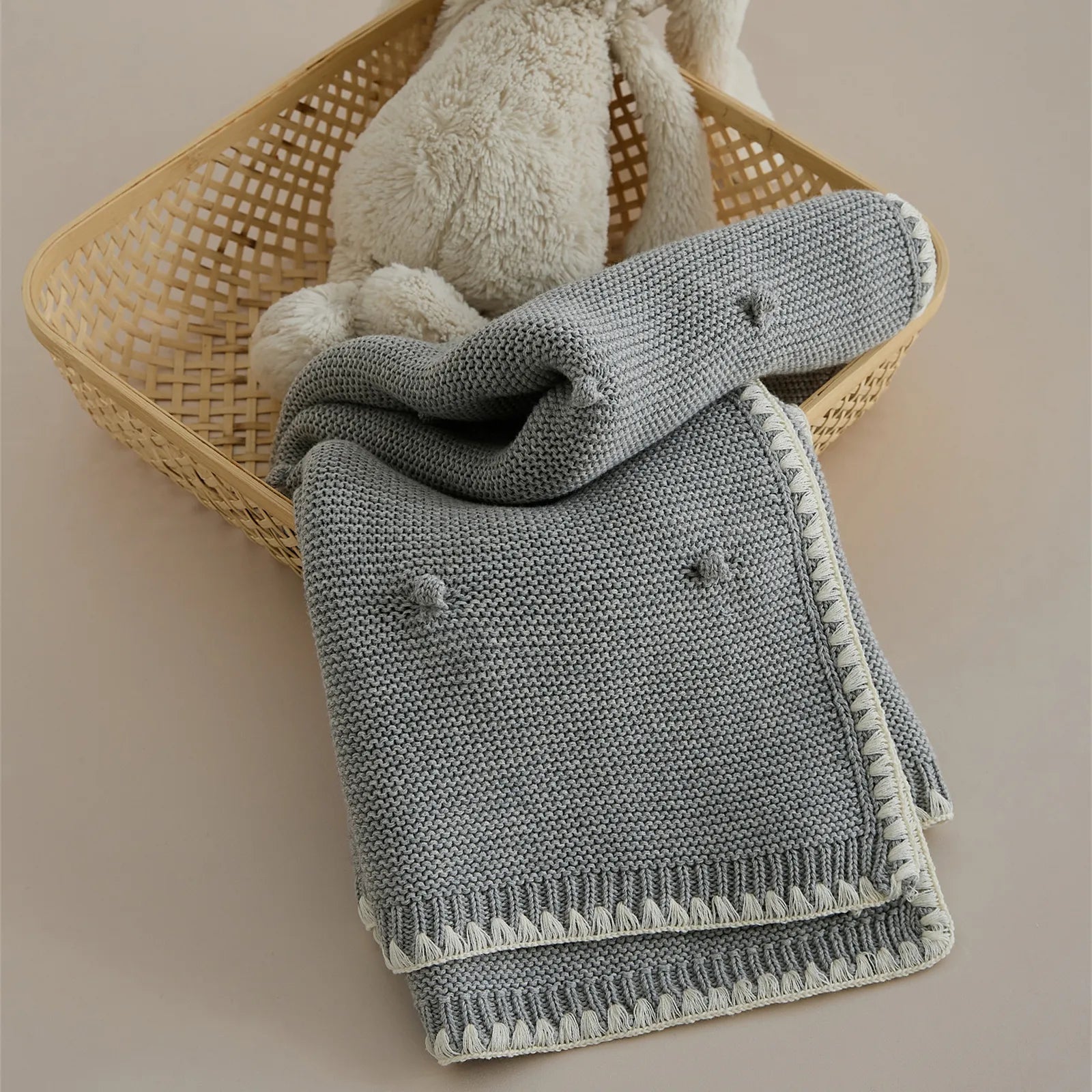 Medium grey cotton bobble knit throw folded inside a bamboo basket next to a white plush toy