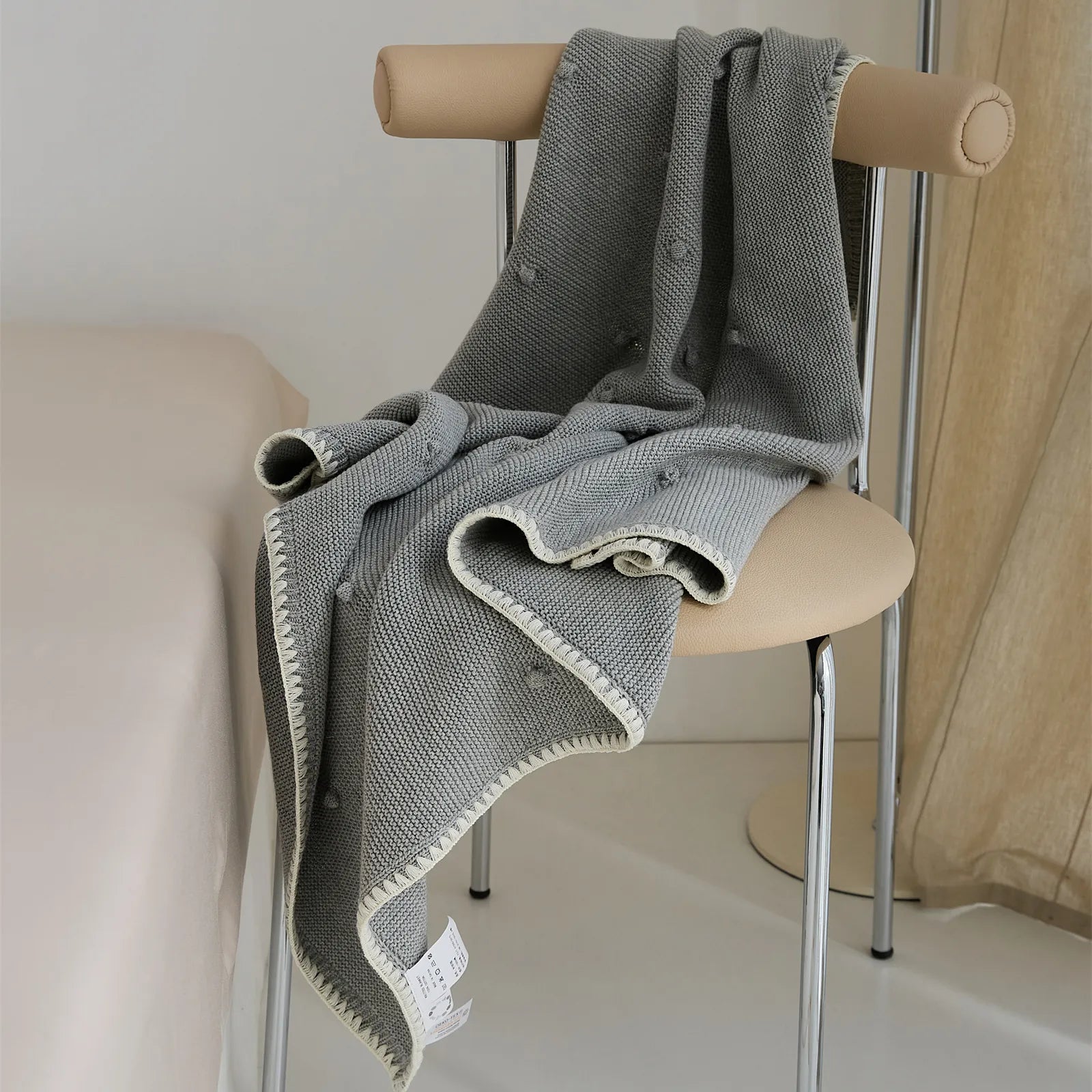 Medium grey cotton knit throw with cream trim draped over a modern chair in a bedroom