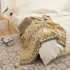 Mustard yellow boho knit throw blanket with tassels draped over a white bed full room view
