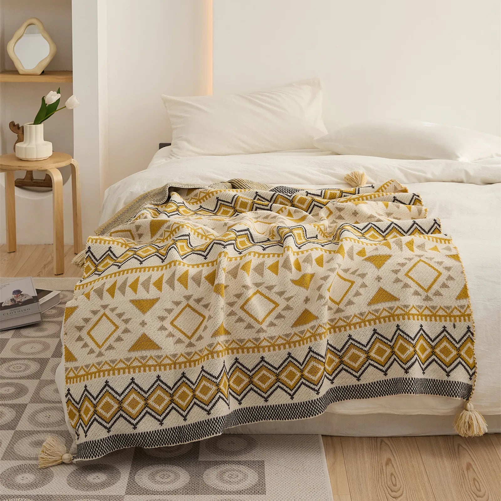 Mustard yellow boho knit throw blanket with tassels spread over a white bed close up view