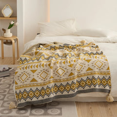 Mustard yellow boho knit throw blanket with tassels spread over a white bed close up view