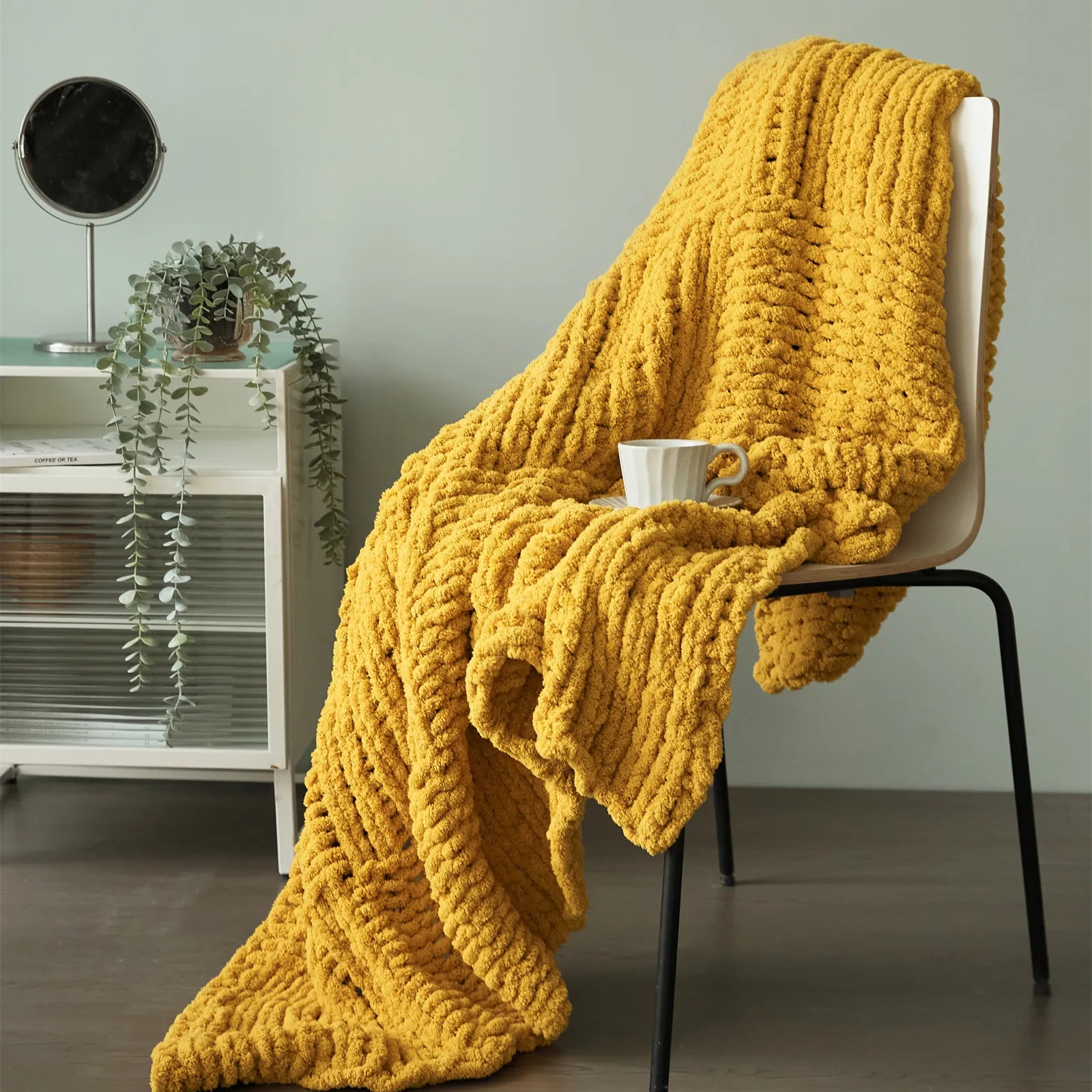 A plush mustard yellow chunky knit blanket draped over a chair, styled with a coffee cup for a cozy, inviting look.