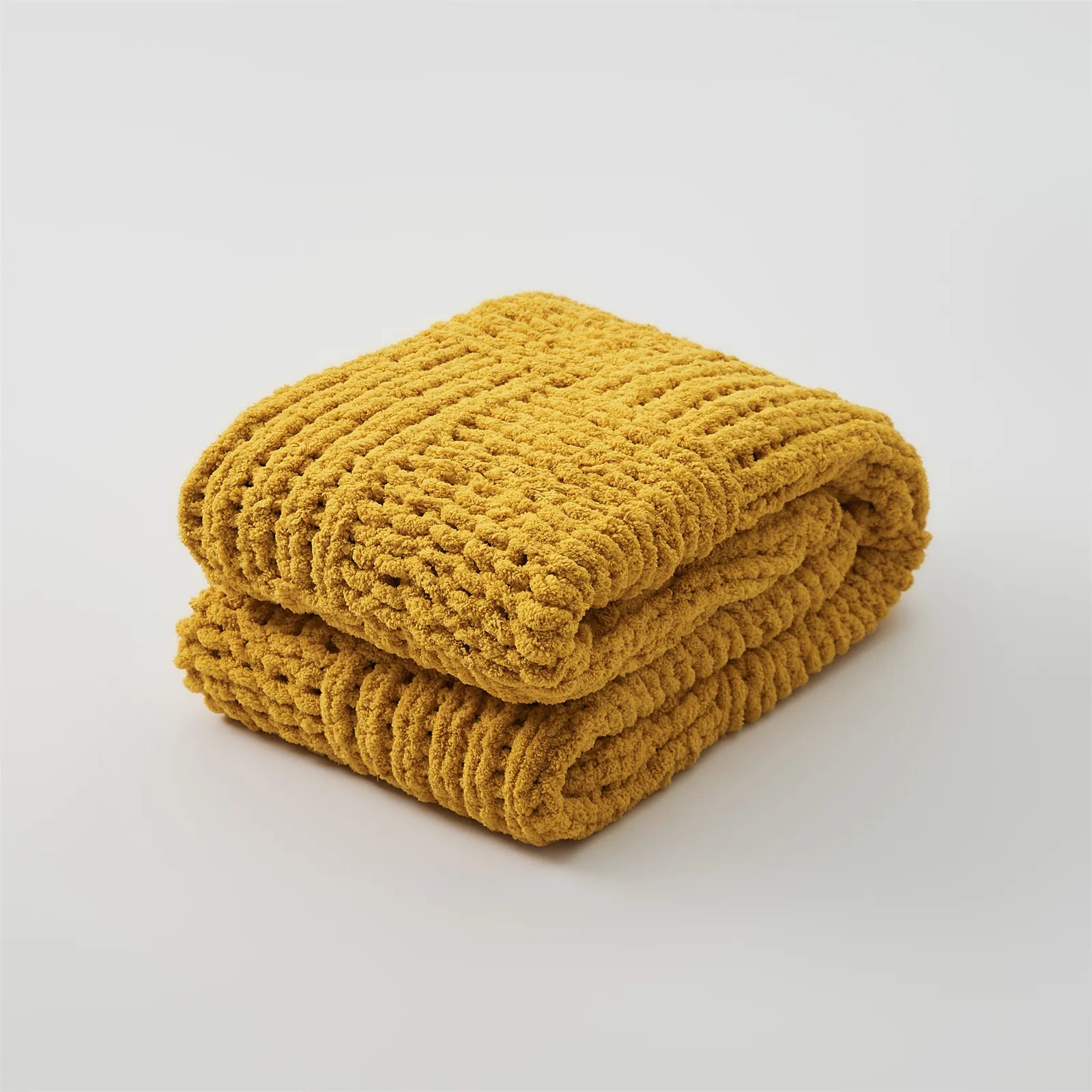 A neatly folded mustard yellow chunky knit blanket shown in a studio setting, emphasizing its texture and color.