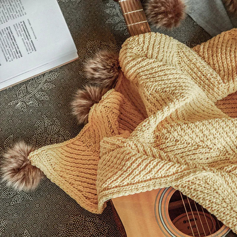 Mustard yellow pom-pom throw draped over an acoustic guitar and open book