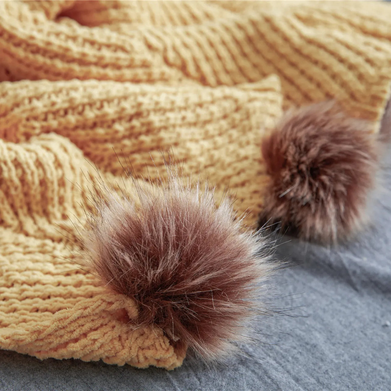 Close up detail of soft mustard yellow knit fabric and large brown faux fur pom-pom