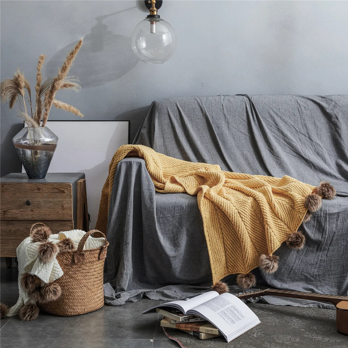 Mustard yellow pom-pom throw draped on grey sofa in bohemian living room