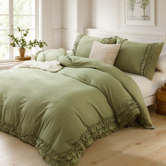 Olive green cotton double ruffle duvet cover and pillows on a bed with a plant on the windowsill and a wooden cabinet.